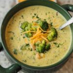 Bowl of high protein broccoli cheddar soup with melted cheese and fresh broccoli florets