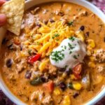 Bowl of high protein creamy taco soup topped with cheese, cilantro, and tortilla chips