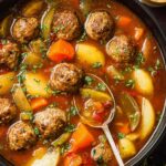 Hearty meatball stew in a white bowl with tender meatballs, potatoes, carrots, and peas in rich brown gravy