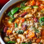 Bowl of minestrone with sausage garnished with basil pesto and parmesan cheese