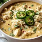 Bowl of crockpot creamy white chicken chili topped with avocado sour cream and tortilla strips