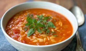 Hearty tomato orzo soup in white bowl garnished with fresh basil