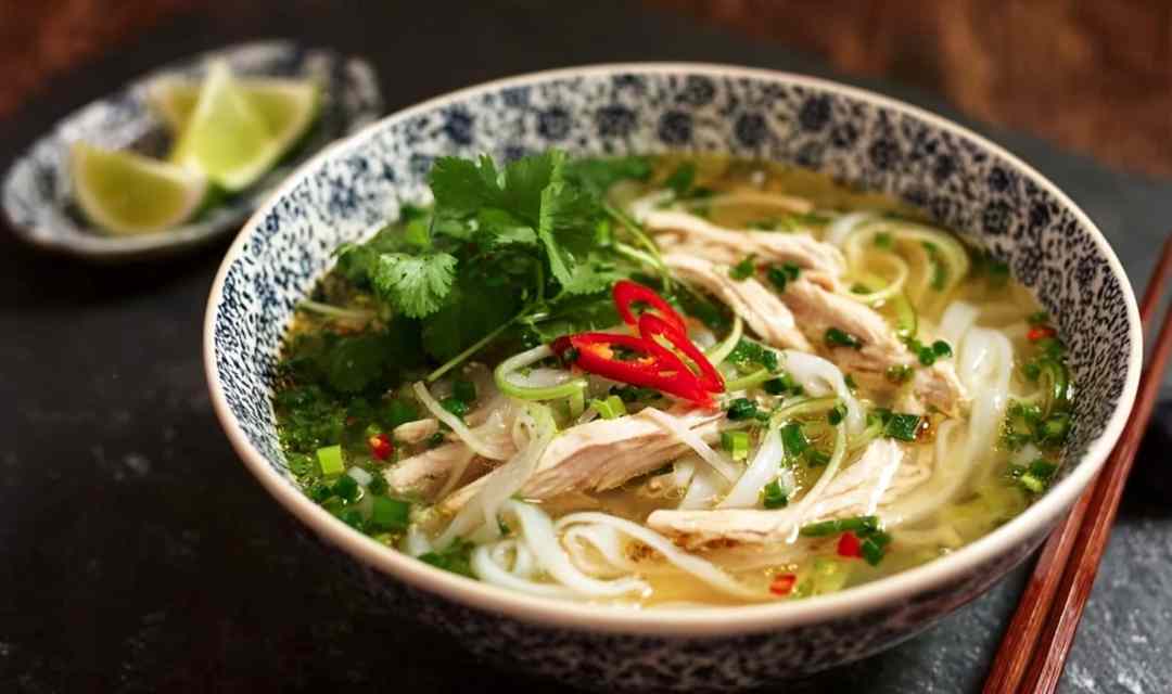 Bowl of Pho Ga Vietnamese Chicken Noodle Soup with clear golden broth, rice noodles, and fresh herbs