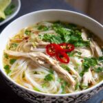 Bowl of Pho Ga Vietnamese Chicken Noodle Soup with clear golden broth, rice noodles, and fresh herbs