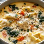 White lasagna soup in a large pot with melted cheese, Italian sausage, and fresh basil garnish
