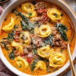 Butternut squash sausage tortellini soup in white bowl with parmesan cheese garnish