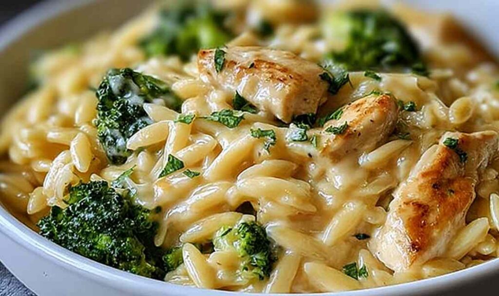 Cheesy chicken broccoli orzo in a large skillet with melted cheddar cheese and tender broccoli florets