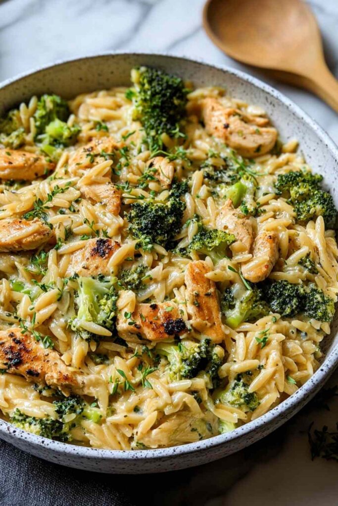Cheesy chicken broccoli orzo in a large skillet with melted cheddar cheese and tender broccoli florets