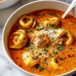 Cheesy tomato tortellini soup in white bowl garnished with Parmesan cheese and basil