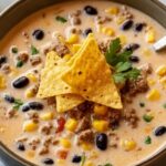 Creamy Cowboy Soup in white bowl topped with green onions and shredded cheese