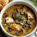 Bowl of creamy rotisserie chicken mushroom soup garnished with fresh parsley on white background