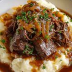 Slow cooker French onion pot roast with shredded beef in rich brown gravy served over mashed potatoes