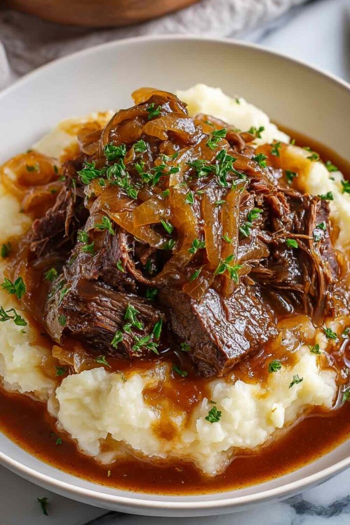 Slow cooker French onion pot roast with shredded beef in rich brown gravy served over mashed potatoes