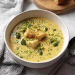 Bowl of creamy smoked gouda broccoli soup garnished with croutons and extra cheese
