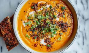 Spicy miso carrot soup in white bowl garnished with green onions and cilantro