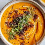 Spicy miso carrot soup in white bowl garnished with green onions and cilantro