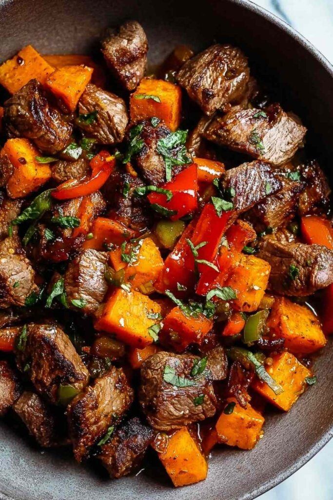 Colorful plate of steak bites with sweet potatoes and peppers garnished with fresh parsley