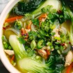 Bok choy chicken soup in white bowl with chopsticks and lime wedges
