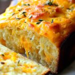Sliced cheddar cheese quick bread on wooden cutting board showing fluffy texture