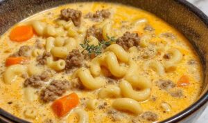 Bowl of cheeseburger macaroni soup topped with shredded cheddar cheese and diced pickles