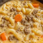 Bowl of cheeseburger macaroni soup topped with shredded cheddar cheese and diced pickles