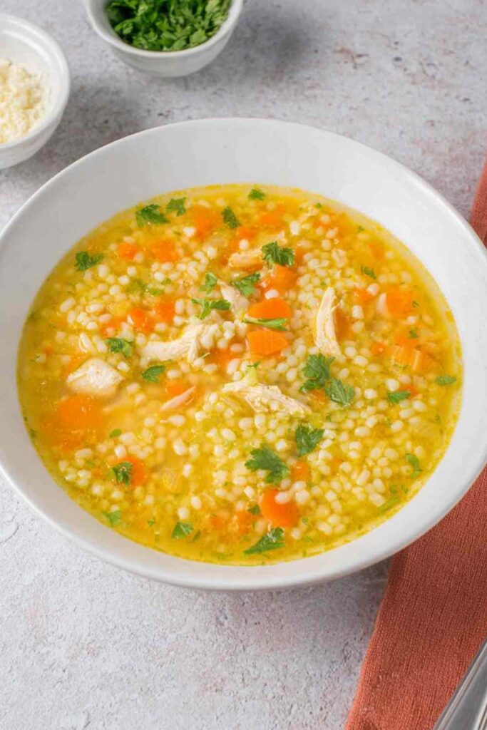 Bowl of chicken pastina soup with tiny pasta, shredded chicken, and vegetables in golden broth topped with Parmesan cheese