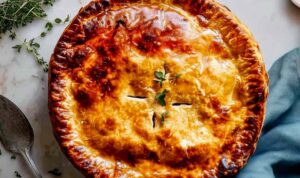 Golden chicken pot pie recipe with flaky crust on white plate showing creamy filling