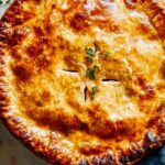 Golden chicken pot pie recipe with flaky crust on white plate showing creamy filling