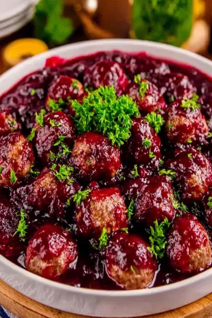 Cranberry meatballs in slow cooker with glossy red sauce garnished with fresh herbs