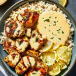 Creamy lemon butter chicken with crispy zucchini rounds and couscous on a white plate