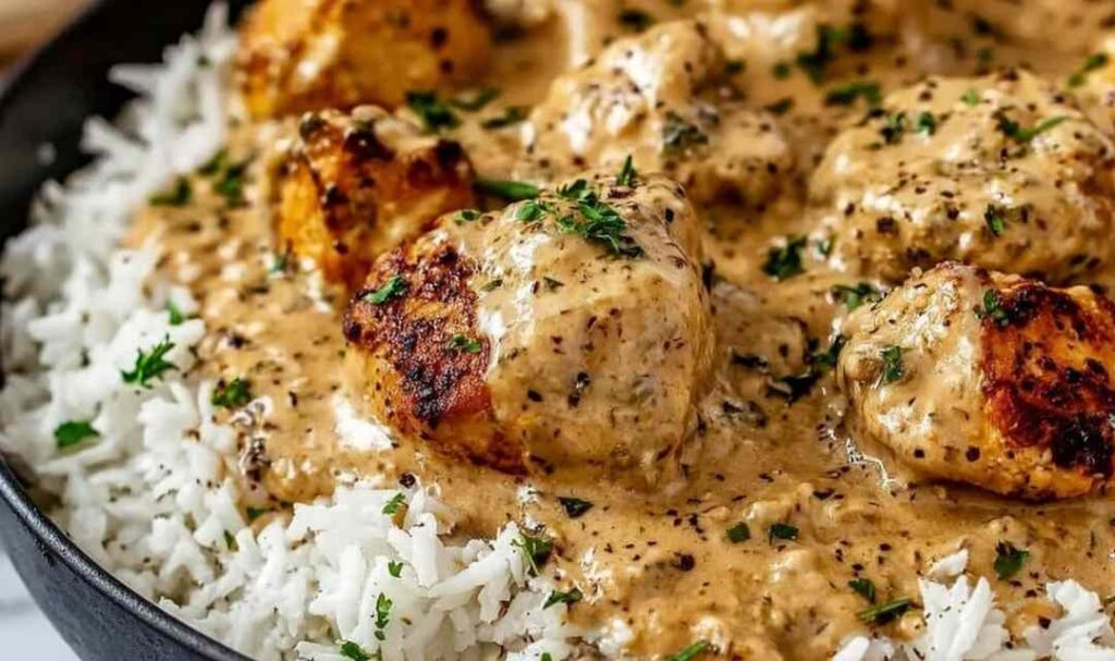 Creamy smothered chicken and rice on a white plate with parsley garnish