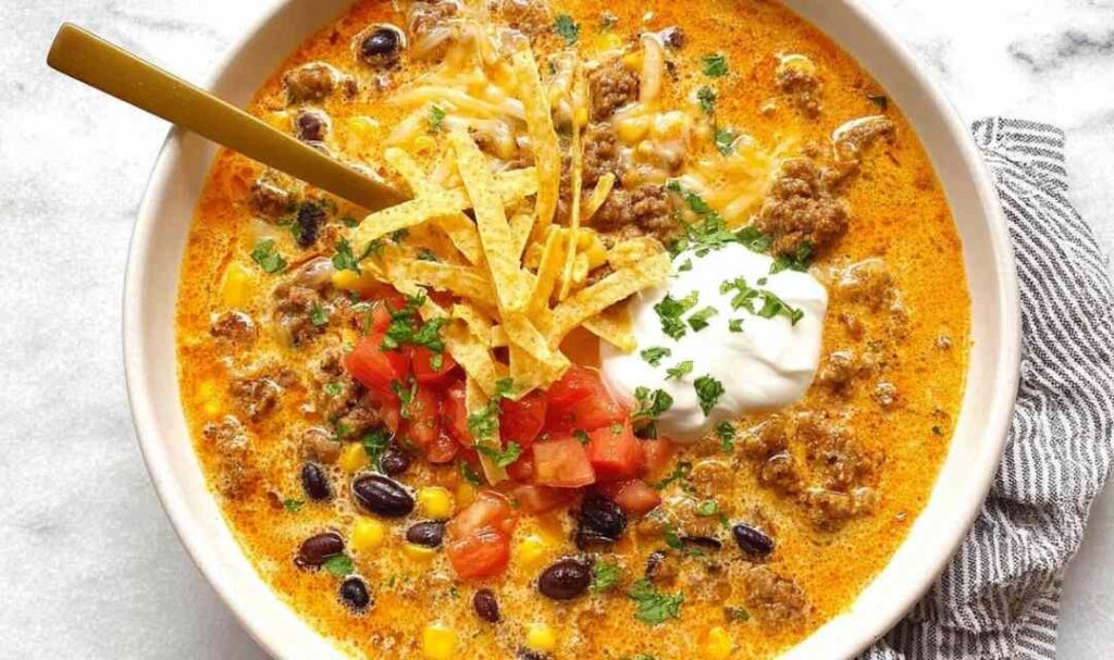 Bowl of creamy taco soup topped with shredded cheese, sour cream, and tortilla chips