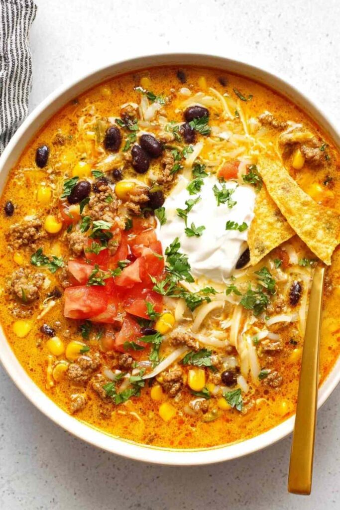 Bowl of creamy taco soup topped with shredded cheese, sour cream, and tortilla chips