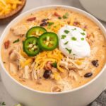 Bowl of crock pot cream cheese chicken chili topped with shredded cheese and cilantro