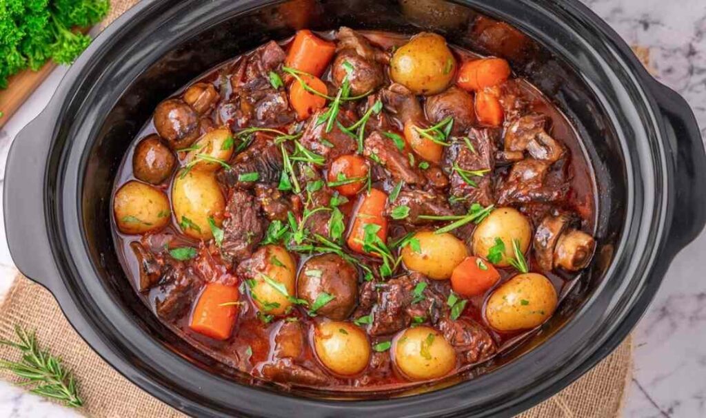 Crockpot beef bourguignon in slow cooker with tender beef chunks, carrots, pearl onions and mushrooms in rich red wine sauce