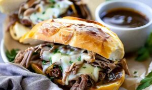 Crockpot French Dip Sandwiches with melted provolone cheese and au jus for dipping