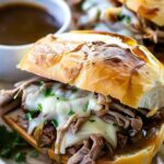 Crockpot French Dip Sandwiches with melted provolone cheese and au jus for dipping