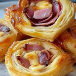 Golden Ham and Cheese Puff Pastry Pinwheels arranged on white serving platter showing flaky layers and melted cheese