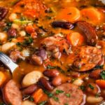 Hearty bean soup with smoked sausage in white bowl with crusty bread