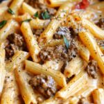 One pot creamy tomato beef pasta in large pot with wooden spoon and fresh basil garnish
