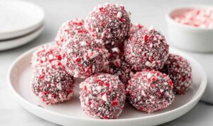 Peppermint Oreo Balls coated in white chocolate with crushed candy canes on top arranged on a festive holiday plate