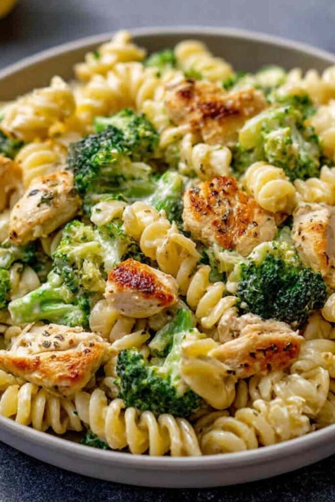 Rotisserie Chicken Broccoli Pasta in white bowl with fork showing creamy sauce coating pasta and bright green broccoli