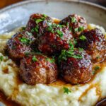 Salisbury steak meatballs with garlic herb mashed potatoes covered in mushroom gravy on white plate