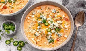 Slow cooker buffalo chicken chili in white bowl topped with cheese and green onions