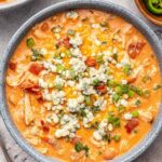 Slow cooker buffalo chicken chili in white bowl topped with cheese and green onions