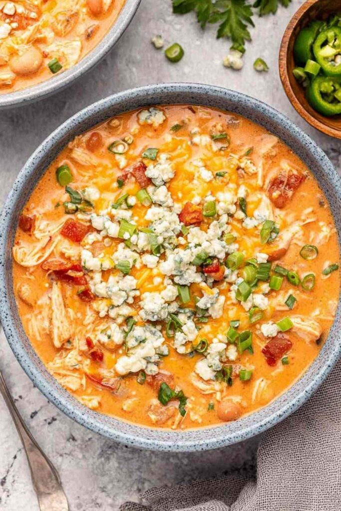 Slow cooker buffalo chicken chili in white bowl topped with cheese and green onions