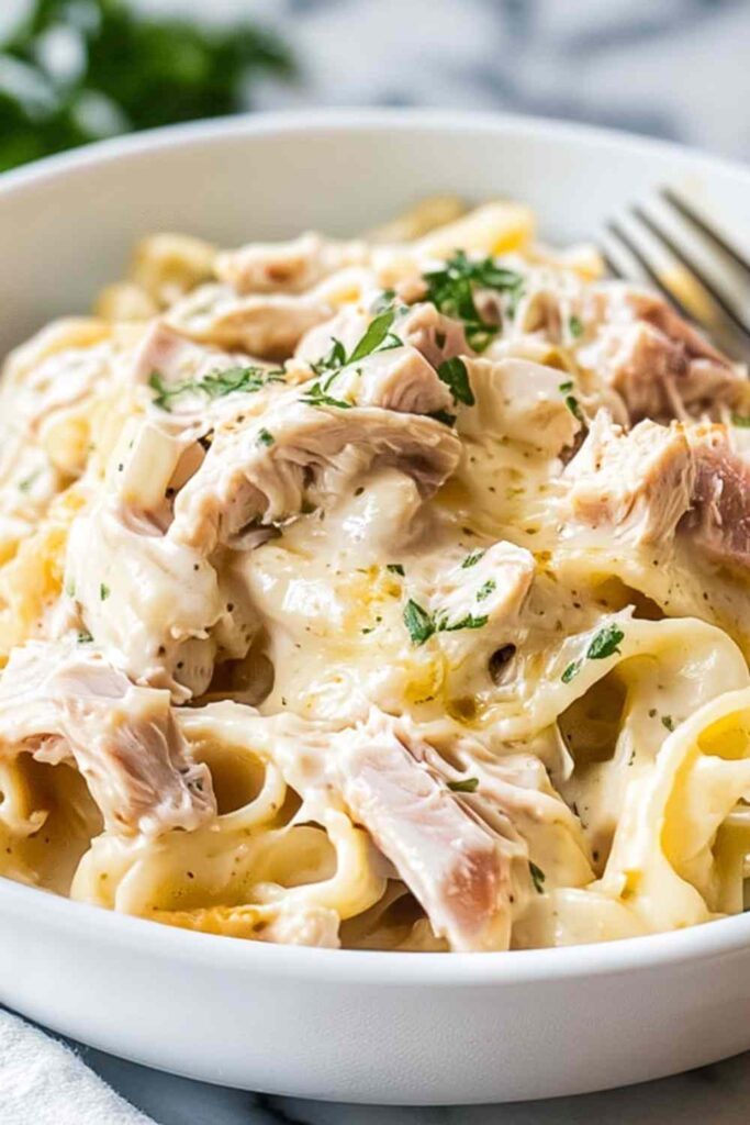 Slow Cooker Chicken Cordon Bleu Pasta in white bowl with creamy sauce and melted Swiss cheese
