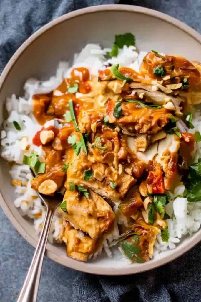 Slow Cooker Peanut Chicken in white bowl garnished with crushed peanuts and cilantro