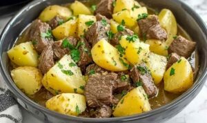 Slow cooker steak and cheddar potato casserole in white bowl with melted cheese and fresh parsley garnish