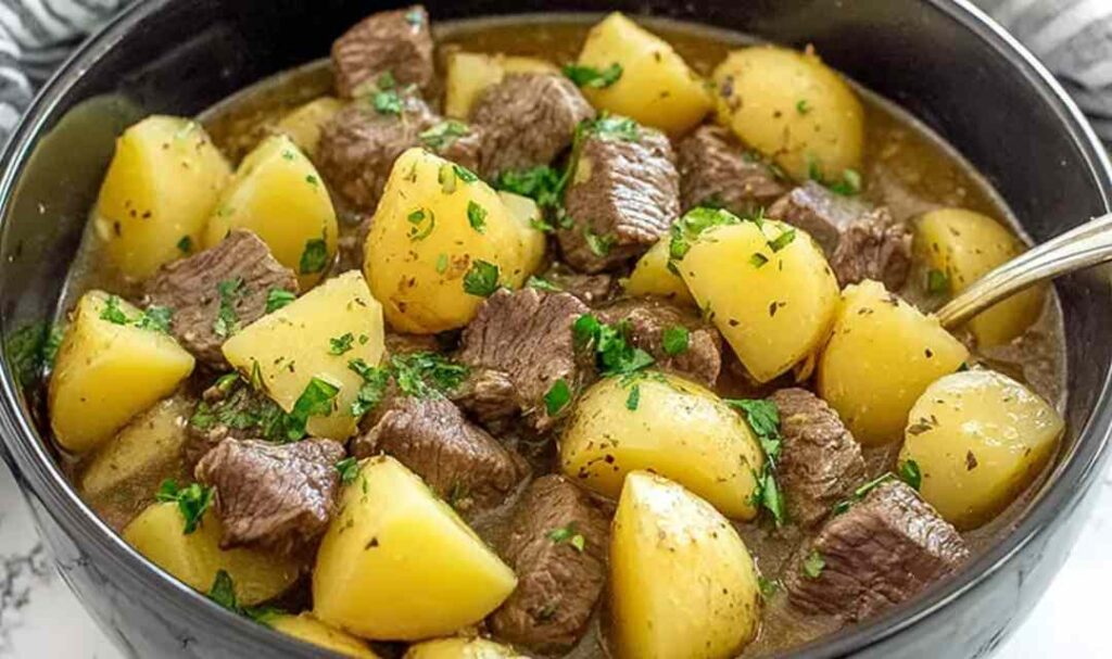Slow cooker steak and cheddar potato casserole in white bowl with melted cheese and fresh parsley garnish